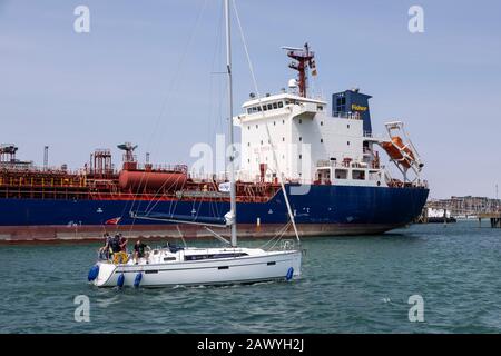 Le pétrolier "Cumbrian Fisher" éclipse un yacht qui passe dans le port de Portsmouth, Au Royaume-Uni. Banque D'Images