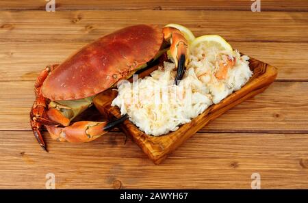 Crabe brun frais entier et viande fraîche dans un plat en bois sur fond de bois avec citron Banque D'Images