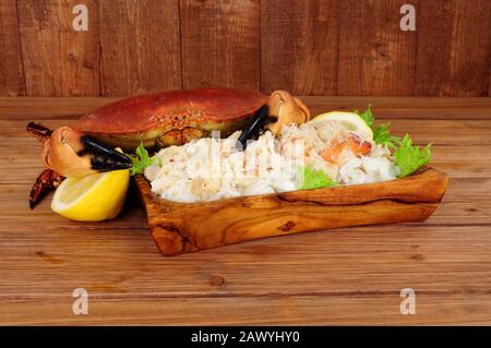 Crabe brun frais entier et viande fraîche dans un plat en bois sur fond de bois avec citron Banque D'Images