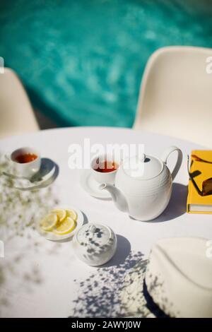 Service de thé sur la table ensoleillée de terrasse en bordure de piscine en été Banque D'Images