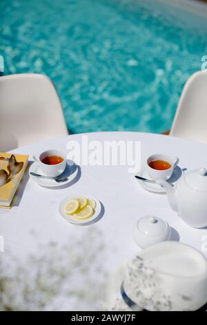 Service de thé sur la table ensoleillée de terrasse en bordure de piscine en été Banque D'Images