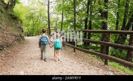 Les petits touristes les garçons et les filles tenant les mains vont au camping familial le long d'une route de la forêt de gravier dans les Alpes montagnes. Les enfants avec des sacs à dos vont sur un hiki Banque D'Images