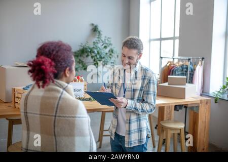 Jeune homme riant écrire note tout en parlant à la fille. Banque D'Images