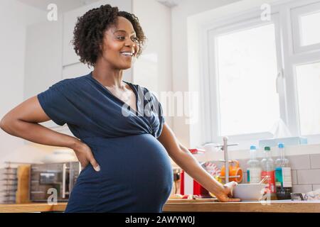Bonne femme enceinte qui mange dans la cuisine Banque D'Images