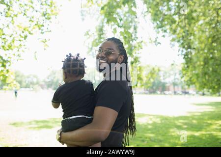 Portrait heureux père avec de longues tresses tenant le petit enfant dans le parc Banque D'Images