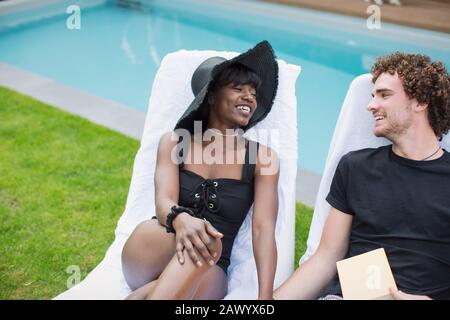 Un jeune couple heureux se détendant dans des chaises longues au bord de la piscine Banque D'Images