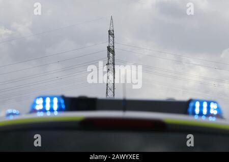 Duisburg, Allemagne. 10 février 2020. Une voiture de police à lumière bleue se trouve devant un pôle d'alimentation, où il y a un problème avec la ligne haute tension qui s'étend sur le Rhin. Au début, un câble de mise à la terre inoffensif avait chuté dans l'eau du côté de Krefeld, ce qui pourrait éventuellement conduire à un câble sous tension, selon la police de Duisburg. La rivière a été fermée pour le transport entre Düsseldorf et Krefeld. À l'heure actuelle, il ne peut être ni confirmé ni nié si l'affaire comporte des dommages causés par des tempêtes. Crédit: David Young/Dpa/Alay Live News Banque D'Images