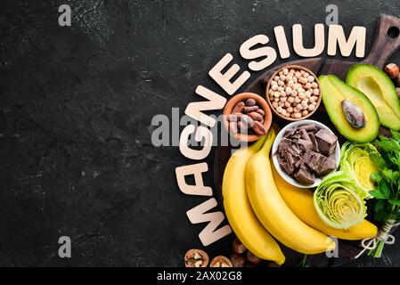 Aliments contenant du magnésium naturel. Mg : chocolat, banane, cacao, noix, avocats, brocoli, amandes. Vue de dessus. Sur fond noir. Banque D'Images