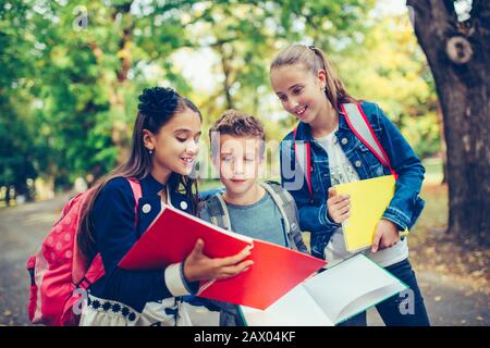 Retour à l'école. Les enfants avec des sacs à dos ont du plaisir, de parler, de lire un livre.Groupe d'écoliers élémentaires ayant une discussion sur les devoirs pendant leur déplacement Banque D'Images