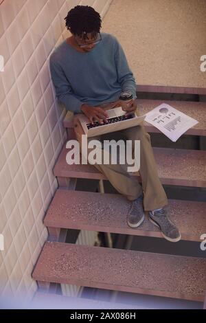 Vue panoramique sur l'homme afro-américain contemporain avec ordinateur portable tout en étant assis sur l'escalier Banque D'Images