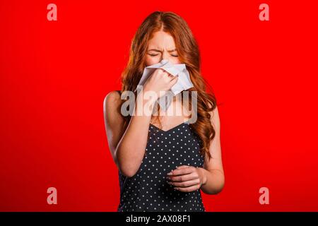 La jeune fille éternue dans le tissu. Isolé sur la femme rouge est malade, a bourré ou liquide nez et fièvre. Coronavirus, épidémie 2020, concept de maladie. Banque D'Images