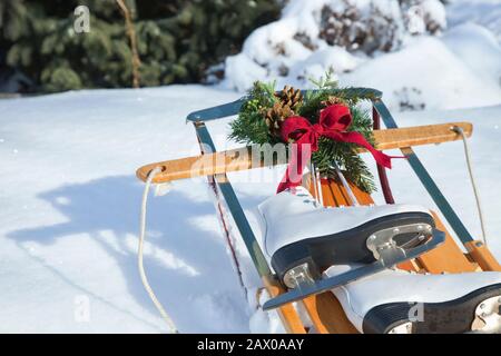 Traîneaux vintage dans la neige avec couronne et noeud rouge et patins blancs le jour ensoleillé Banque D'Images