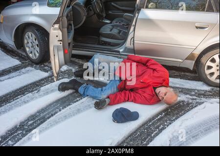 L'homme principal a glissé sur la glace en sortant de sa voiture Banque D'Images