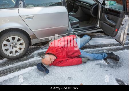 L'homme principal a glissé sur la glace en sortant de sa voiture Banque D'Images