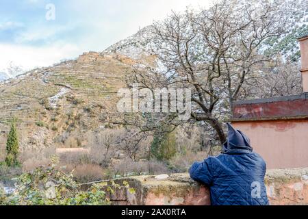 Berber homme reposant sur le bord de la route en vêtements traditionnels avec capuche dans la vallée de l'Ourika, au Maroc Banque D'Images