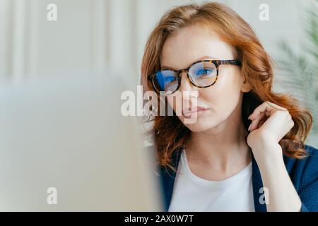 Gros plan de travail de la femme ciblée termine le projet réussi, fait le travail à distance, focalisé sur le moniteur de l'ordinateur portable, porte des lunettes optiques pour Banque D'Images