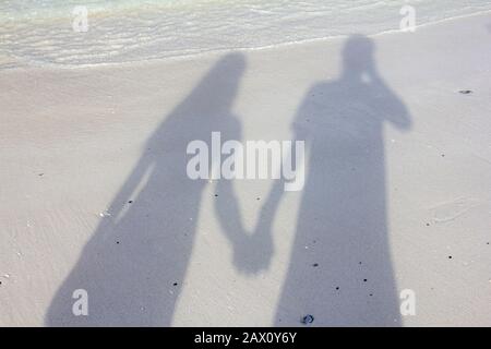 Ombre d'un couple heureux tenant les mains le long de la plage pendant le coucher du soleil Banque D'Images