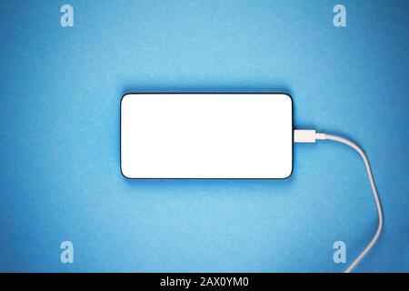 maquette d'un nouveau smartphone avec un écran blanc avec un fil de chargeur blanc sur fond bleu gros plan avec une vignette Banque D'Images