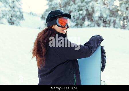 Stock photo d'une jeune fille riant tout en tenant son snowboard sur une montagne enneigée Banque D'Images