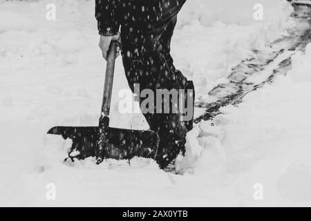 un homme nettoie le sentier neigeux en hiver avec une pelle en neige, noir et blanc Banque D'Images