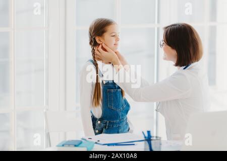 Photo de la pédiatre féminine examine les childs gorge, étant professionnel spécialisé pédiatre, consulte les enfants comment empêcher la amygdalite, donne de bons arbres Banque D'Images