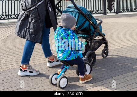 une jeune mère avec une poussette de bébé et un bébé garçon sur un promon marche le long du trottoir de la ville Banque D'Images