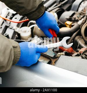Ingénieur mécanicien de voiture utilisant une clé en cours de fixation d'une voiture. Mains mâles de mécanicien de voiture avec une clé qui travaille dans le garage. Homme en gants travaillant dans Banque D'Images