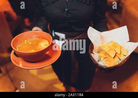 Une serveuse portant un tablier et une cravate servant un bol de soupe chaude et de pain frais Banque D'Images