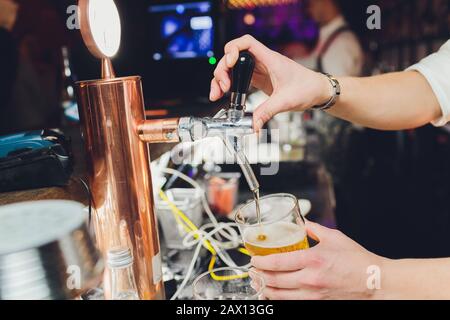 Close up d'un mâle de la bière à la distribution de barman dans un pub et tenant un grand verre tankard sous un robinet pièce jointe sur un fût en acier inoxydable. Banque D'Images