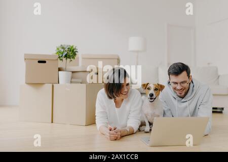 Les couples en famille prennent une pause dans leur nouvel appartement après s'être déplacé, se trouve au rez-de-chaussée et surfer sur Internet par ordinateur portable, posez dans la spacieuse salle lumineuse avec Banque D'Images