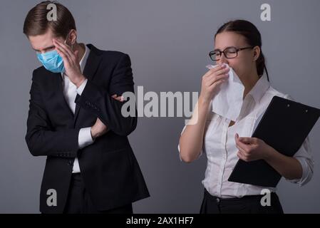 Portrait de deux jeunes hommes d'affaires en vêtements d'affaires. Le gars masqué couvre son visage avec sa main, craignant l'infection par une fille malade. Qui éternue moi Banque D'Images