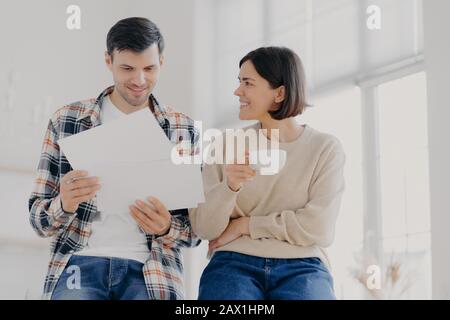 Les gens, les finances et le concept de colluboation. Un couple familial européen heureux analyse les documents ou les conditions du contrat, travaille avec la documentation, femme boit cof Banque D'Images