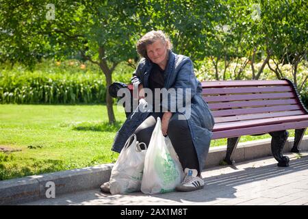 Russie Moscou 2019-06-17 ancienne triste femme assise sur banc avec des sacs en plastique dans le parc à l'extérieur. Concept femme sans abri qui a faim assis seul Banque D'Images