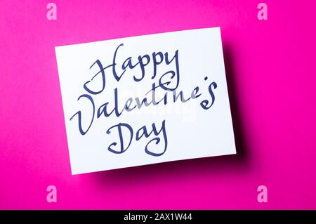 Message manuscrit De Bonne Saint Valentin dans un simple script calligraphique sur carte blanche assise sur fond rose vif Banque D'Images