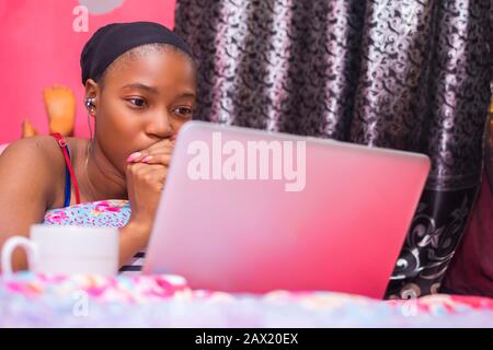 jolie dame africaine à la maison seule dans sa chambre, regarder un film sur son ordinateur portable a l'air effrayé et inconfortable Banque D'Images