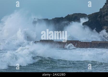 Storm Ciara batte la côte cornouilleuse avec des vagues géantes aussi hautes que les falaises environnantes qui s'écrasent contre le brise-lames Banque D'Images