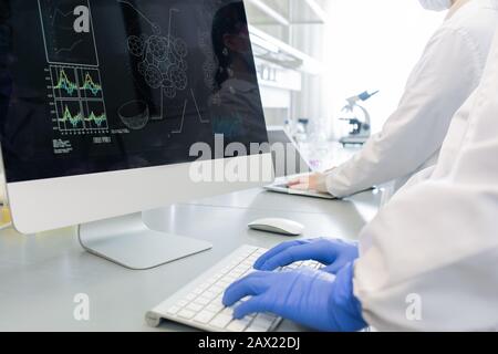 Tir horizontal de deux scientifiques non reconnaissables portant des gants de manteaux blancs travaillant en laboratoire à l'aide d'ordinateurs modernes Banque D'Images