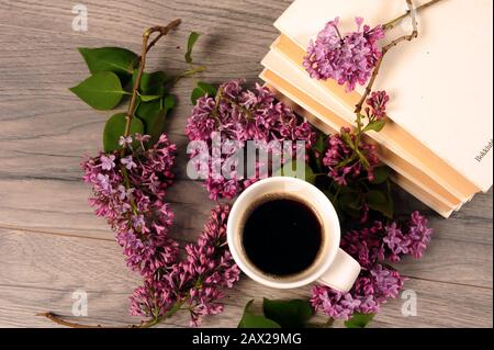 Pile de livres blancs, lilas et tasse blanche avec café noir vu d'en haut. Vue panoramique sur les fleurs et les boissons chaudes. Banque D'Images