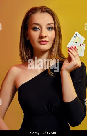 Magnifique blonde femme avec maquillage lumineux, manucure rouge, en robe noire montre deux cartes de jeu, posant sur fond coloré. Jeu Banque D'Images