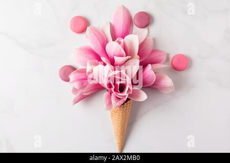 Aménagement créatif réalisé avec des fleurs roses de magnolia dans le cône de gaufres avec macarons sur fond de marbre blanc. Plat. Vue sur le dessus. Mariage ou mariage Banque D'Images