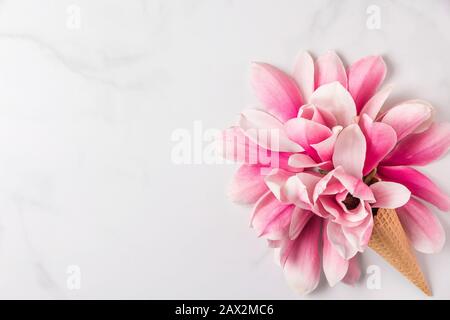 Aménagement créatif réalisé avec des fleurs roses de magnolia dans un cône de crème glacée sur fond de marbre blanc. Plat. Vue sur le dessus. Mariage ou femmes composition de jour. S Banque D'Images