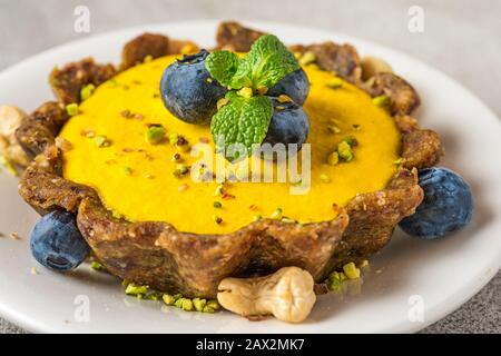 Cheesecake à la mangue brute végétalienne avec bleuets frais, menthe et pistaches. Concept de nourriture sans gluten végétalien sain. Gros plan Banque D'Images