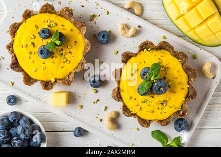 Cheesecakes de mangue brute végétalienne avec baies fraîches, menthe et noix. Concept de nourriture sans gluten végétalien sain. Vue de dessus Banque D'Images