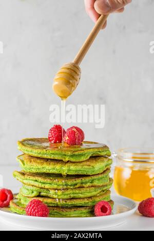 Crêpes vertes au thé de Matcha. Pile de crêpes maison avec framboises fraîches et miel fluide. Bon petit déjeuner dessert. Orientation verticale Banque D'Images