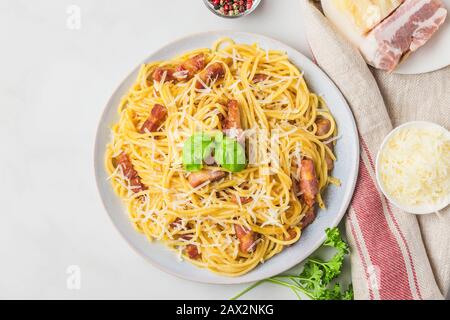 Pâtes italiennes carbonara faites de spaghetti, bacon, parmesan et basilic dans une assiette sur table en marbre blanc. Vue sur le dessus Banque D'Images