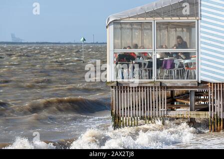 Clients et personnel du restaurant Beach Hut à marée haute et temps de tempête à Southend on Sea, Essex, Royaume-Uni. Affaires sur les fruits de mer au-dessus de l'eau Banque D'Images