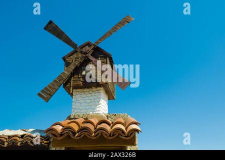 Beau vieux moulin en bois sur un ciel bleu clair dans une journée claire et ensoleillée. Moulin blanc traditionnel décoratif avec un toit marron sur la toiture en tuiles de Banque D'Images