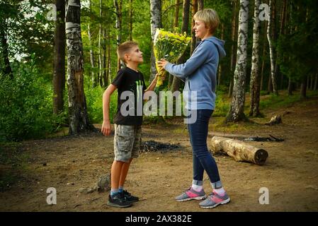 Son donne des fleurs à sa mère dans la nature sur le lac Banque D'Images