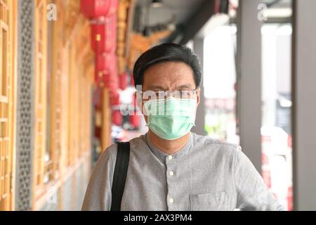 Portrait de l'homme chinois asiatique portant un masque chirurgical. Protection contre le virus ou la brume en extérieur. Banque D'Images