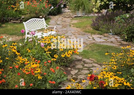 Chemins de flagelès, banc et frontières avec Rudbeckia jaune 'Indian Eté' - Coneflowers avec paveer orange 'Shirley mère de Perle' - fleurs de coquelicot. Banque D'Images